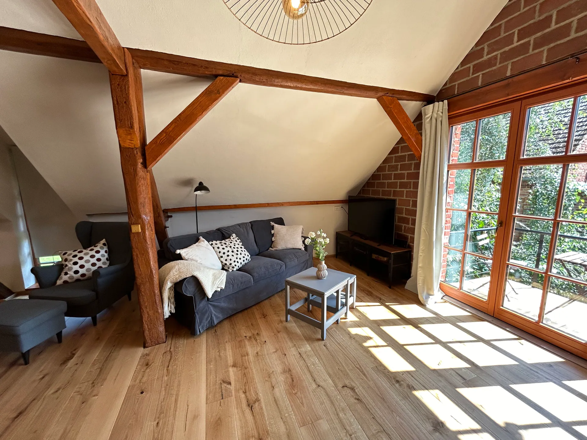 Ferienwohnung III: großzügige Wohnstube mit Sofa, Sichtbalken und Backsteinwand