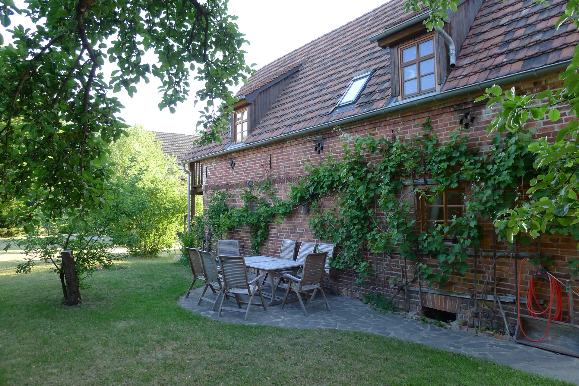 Gartenseite des Ferienhauses mit Gartentisch und Stühlen vor berankter Backsteinwand