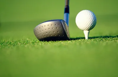 Golfball auf dem Tee neben einem Driver auf kurzem Grün