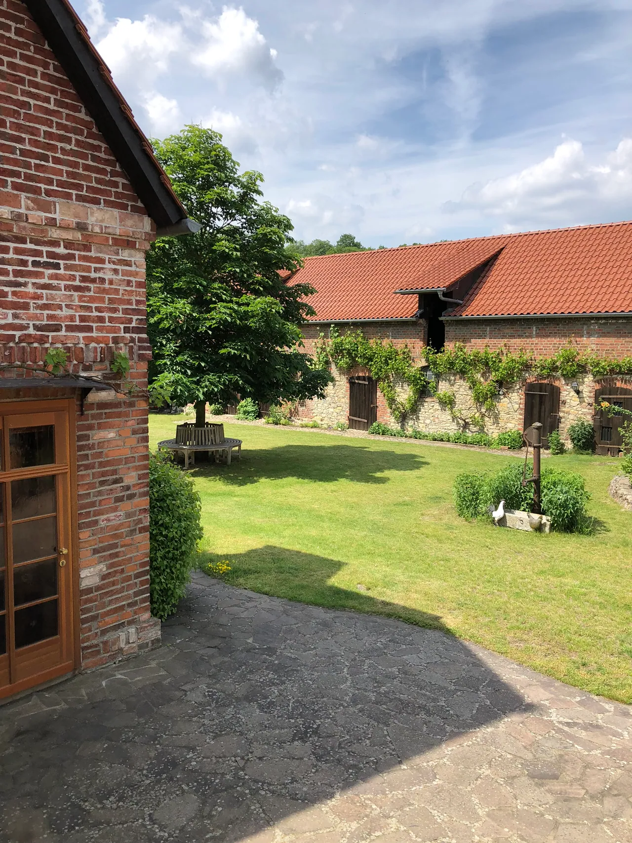 Begrünter Innenhof mit Rundbank unter einem Baum, umgeben von Backsteingebäuden