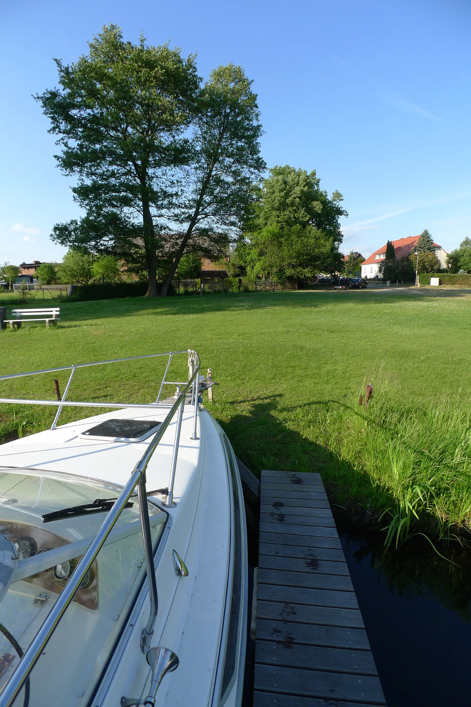 Motorboot am Steg am Spreeufer, dahinter eine Wiese und Häuser