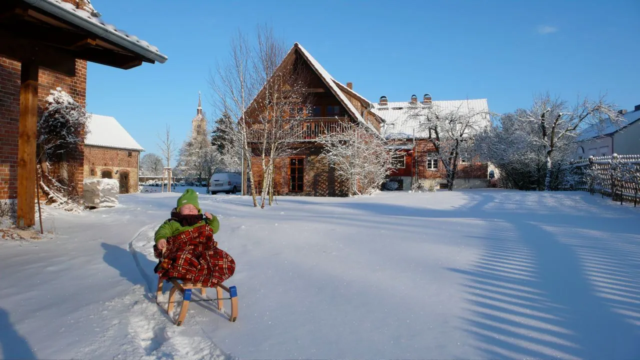 Kind auf dem Schlitten im verschneiten Hof des Ferienhofs